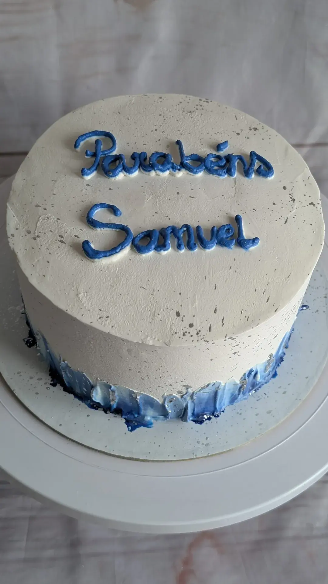 Bolo branco e azul com «Parabéns» escrito em creme